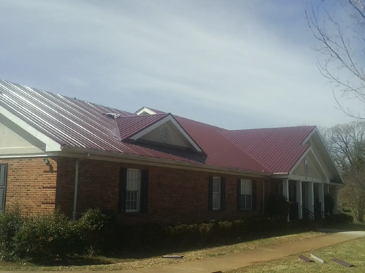 Red metal roof with gabled entries on a long brick building, from a Hail Damage Roof Repair job in North Hills