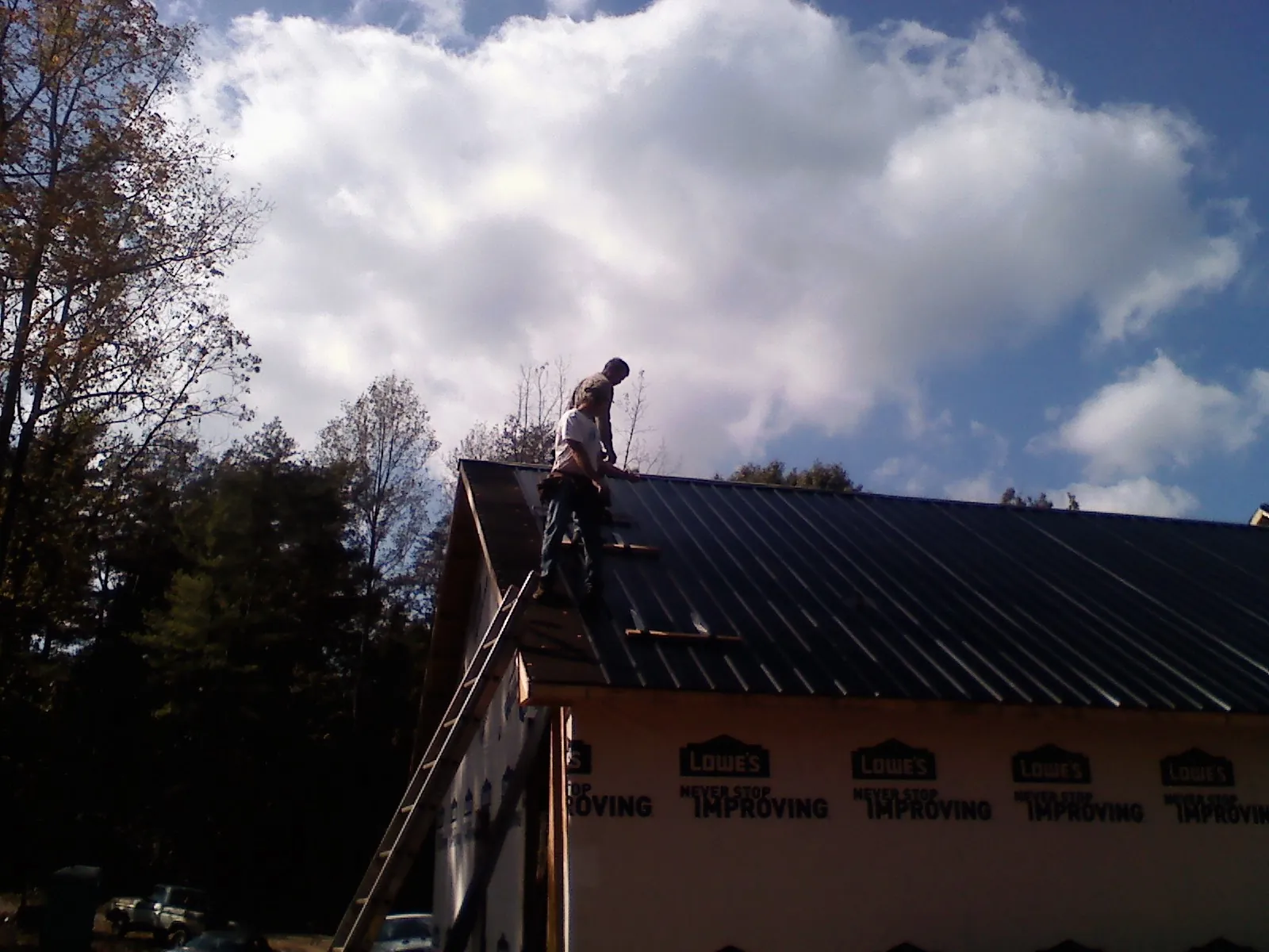 Roofer fastening dark metal panels high against a cloudy sky, from a Roof Inspection job in North Hills