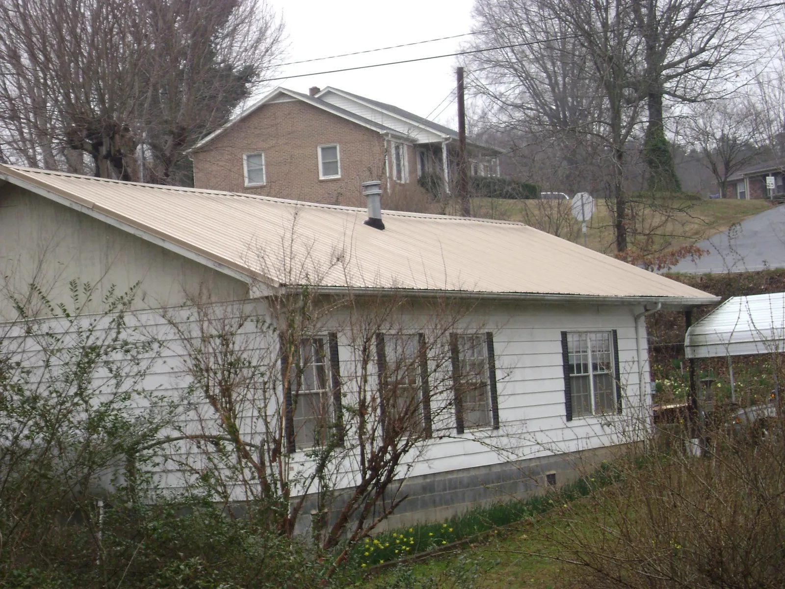 Tan metal roof on a white sided house set into a hillside — Commercial Roofing by Roofing Brothers in North Hills