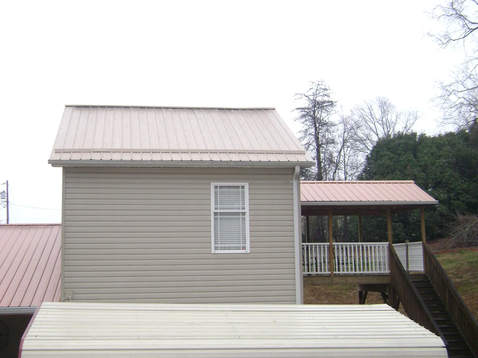 Tan metal roofs on a two story addition and attached porch, from a Roof Replacement job in North Hills